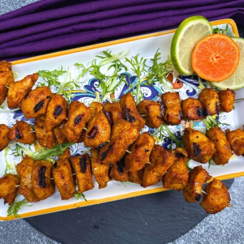 Egyptian chicken kebabs on a white platter with orange and lime slices