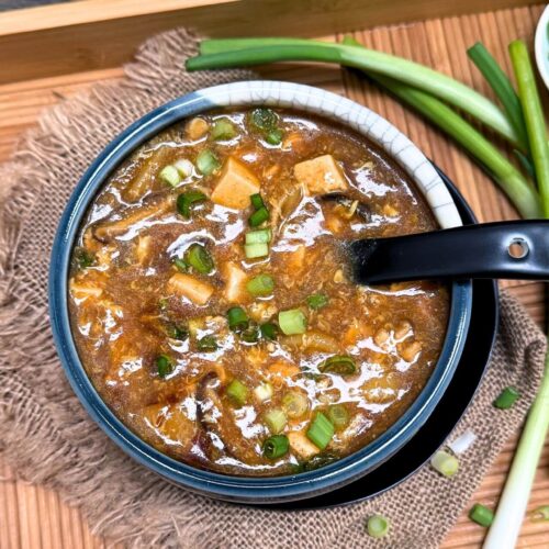 chicken hot and sour soup in a blue bowl with scallions