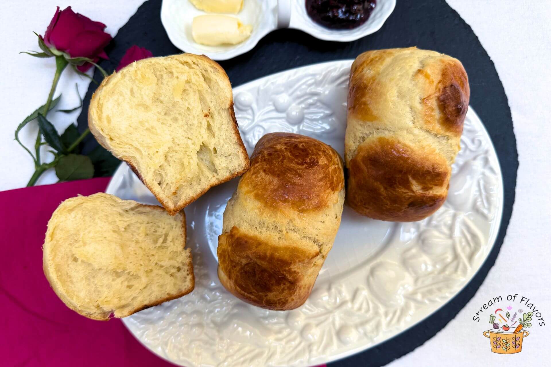 sweet brioche recipe buns on a white platter with butter and jam on the side