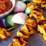 Malaysian chicken satay on a plate with cucumber and katupat