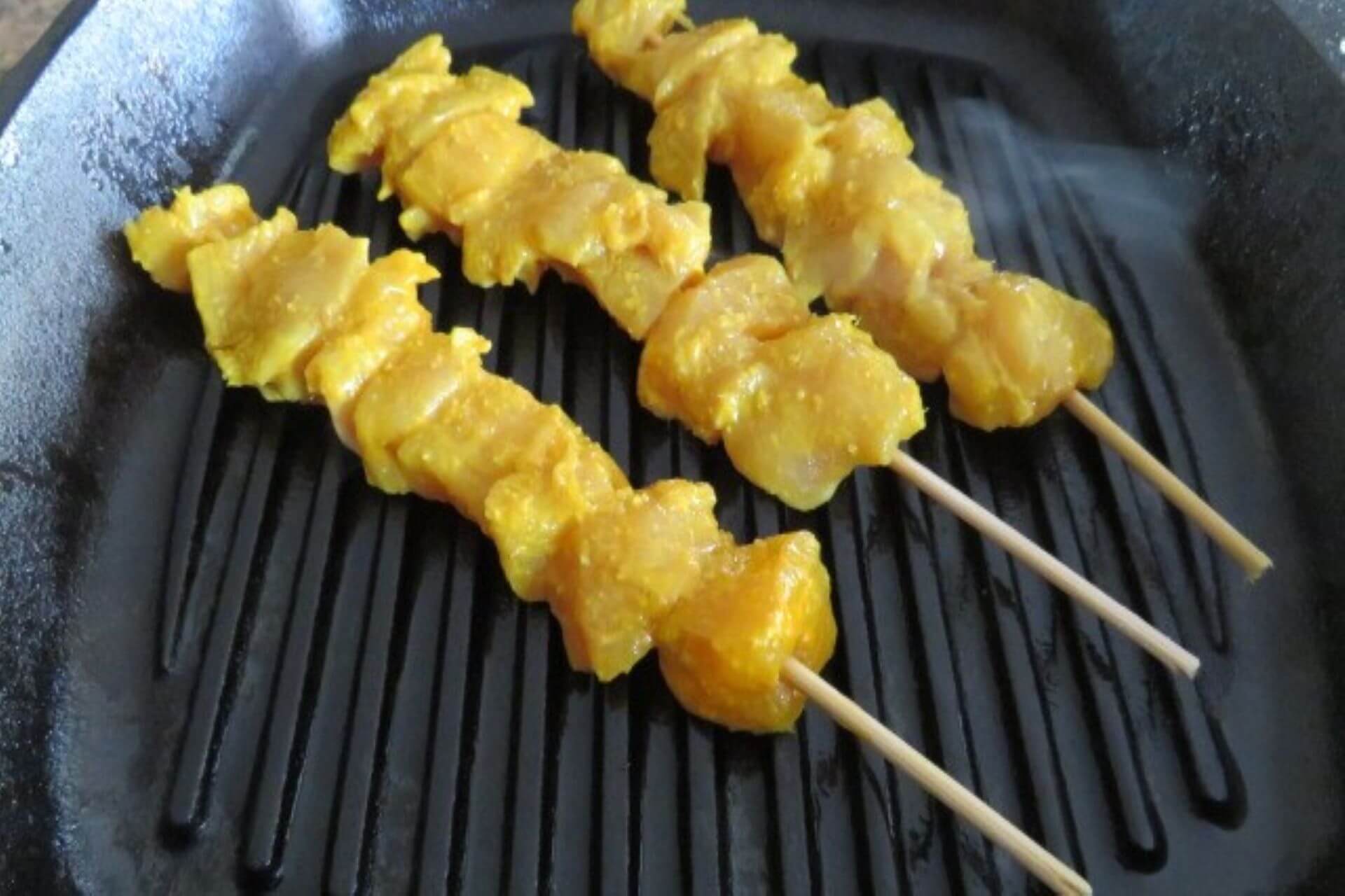 chicken satay grilling on a cast iron skillet