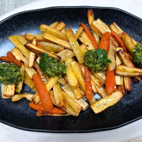 air fryer parsnips and carrots on a black plate with pesto