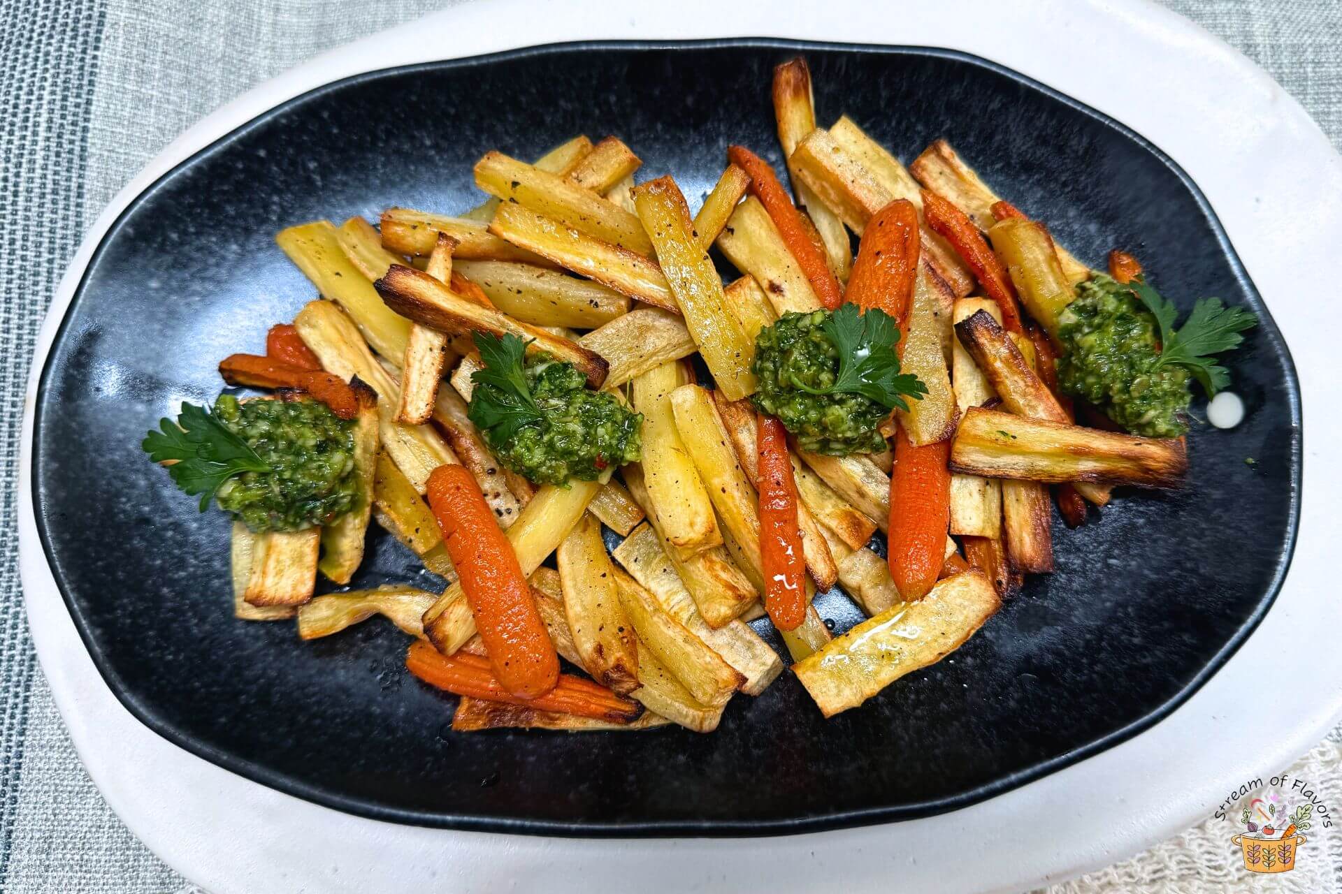 air fryer parsnips and carrots on a black plate with pesto