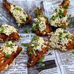 Honey-Glazed Chicken Wings with sesame seeds on a newspaper print garnished with cilantro