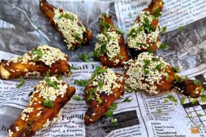 Honey-Glazed Chicken Wings with sesame seeds on a newspaper print garnished with cilantro