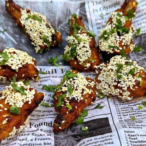 Honey-Glazed Chicken Wings with sesame seeds on a newspaper print garnished with cilantro