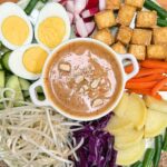gado gado recipe with vegetables, tofu and boiled eggs and peanut sauce in a white bowl