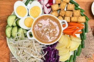 gado gado recipe with vegetables, tofu and boiled eggs and peanut sauce in a white bowl