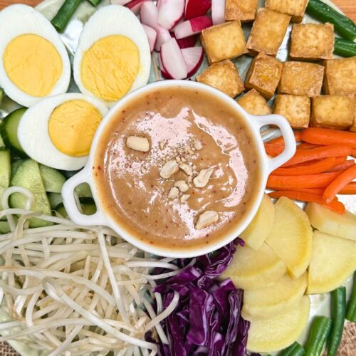 gado gado recipe with vegetables, tofu and boiled eggs and peanut sauce in a white bowl